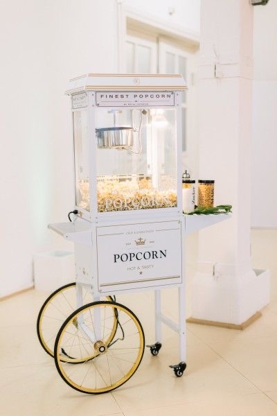 Ein stilvoller, weißer Popcornwagen mit goldenen Akzenten in einem hellen Raum.