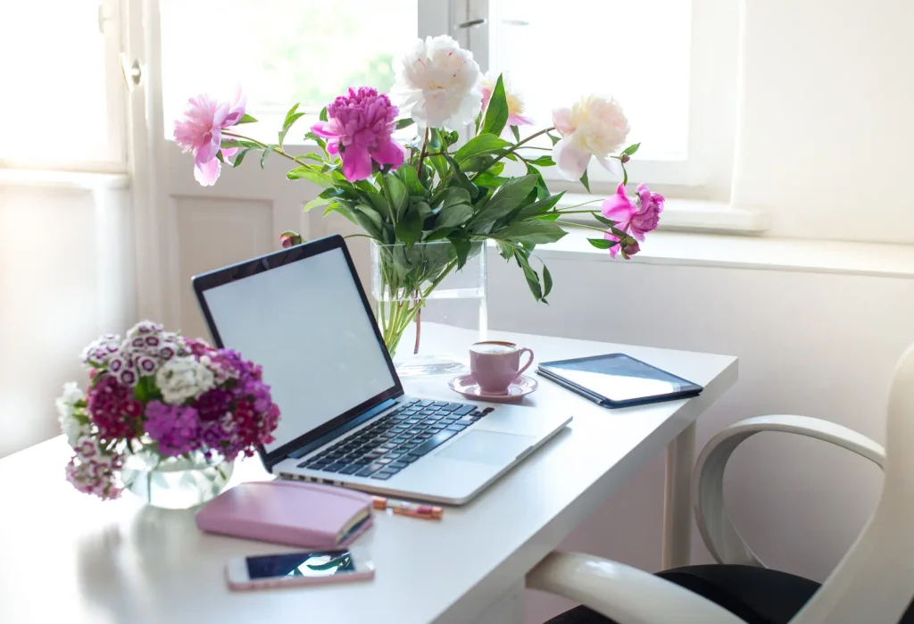 Weisser Schreibtisch mit Laptop Kaffee und rosa Pfingstrosen am Fenster